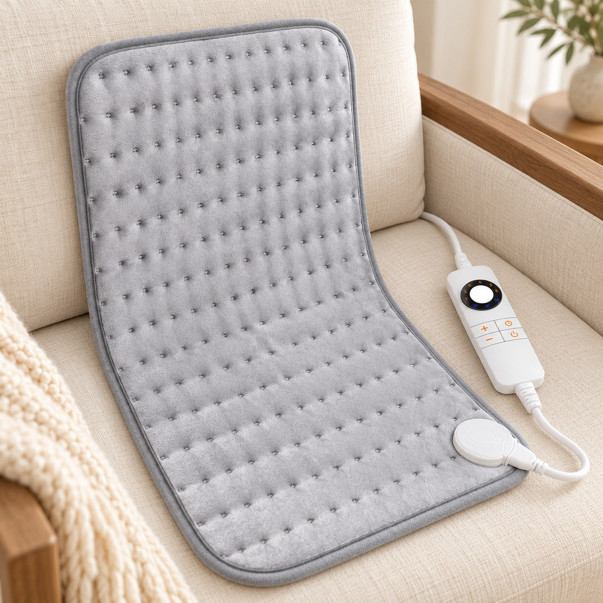 Coussin chauffant gris avec commande blanche sur un fauteuil en lin.